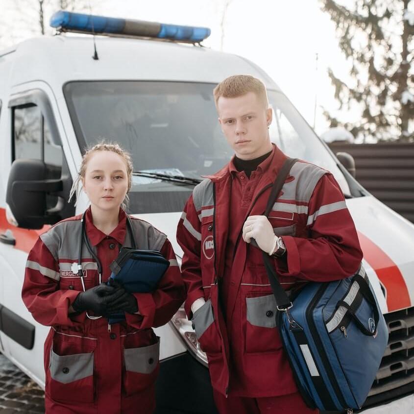 Ženska in moški v opremi zdravstvenega reševalca pred reševalnim vozilom.