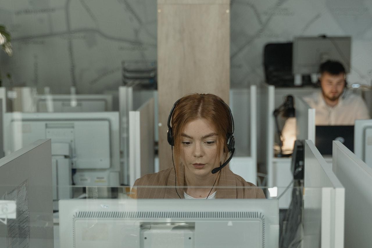 Ženska s slušalkami v klicnem centru sedi pred računalnikom in se pogovarja po telefonu