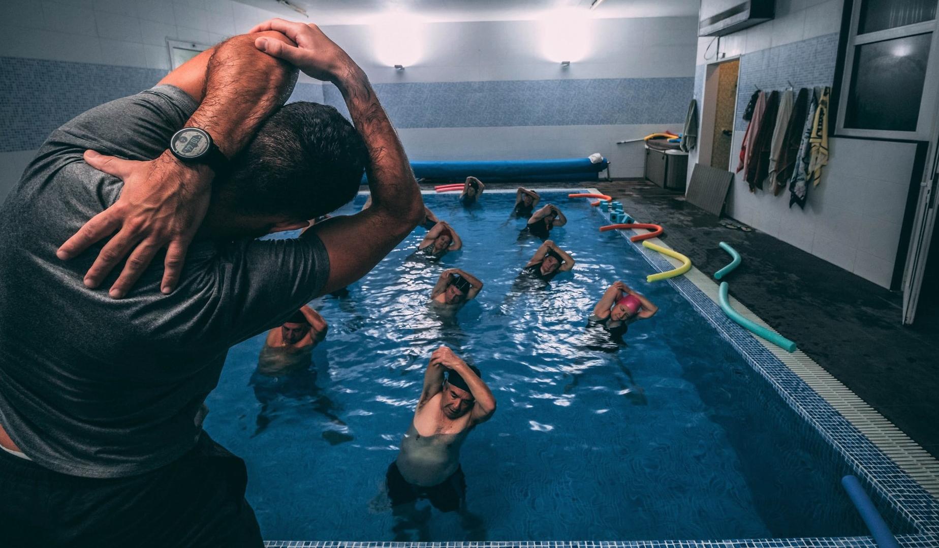 Trener izvaja skupinsko vadbo oseb, ki so v bazenu.
